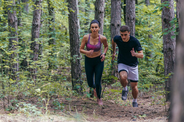 Young athletic couple is running outdoors in the wooded forest area