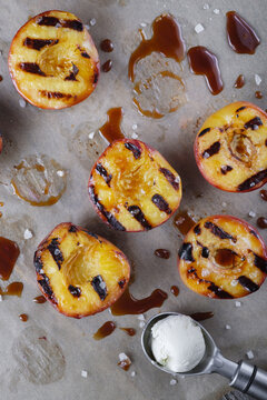  The image of a series about the dessert cooked on the grill. A ball of vanilla ice cream in an ice cream spoon. Ice cream with baked peaches with honey and coarse sea salt.  