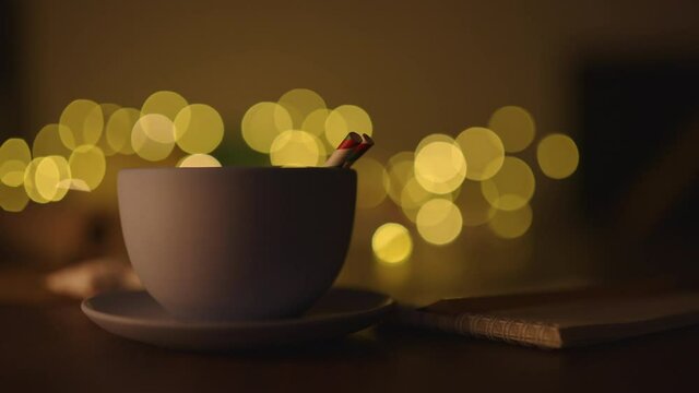 Man hand take blue cup with hot cholate on table with christmas lights on background in dark evening light
