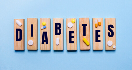 On a light blue background, wooden blocks with the inscription DIABETES and pills. Medical concept