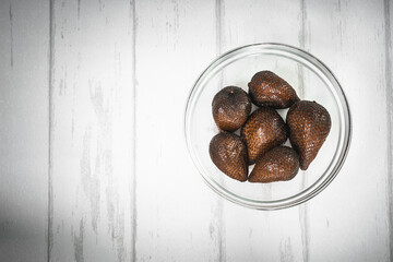 Buah salak or thorny palm or snake fruits on the glass bowl on white wood background
