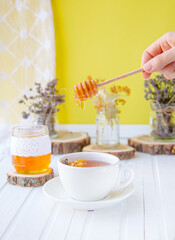 Glass cup of tea with linden in natural organic herbs and a jar of honey on a white wooden table.