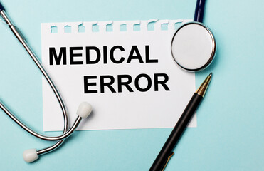 On a light blue background, a stethoscope, a pen and a sheet of paper with the inscription MEDICAL ERROR. Medical concept