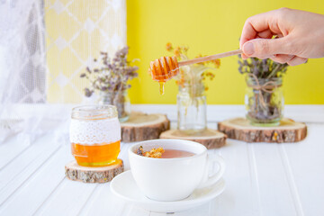 Glass cup of tea with linden in natural organic herbs and a jar of honey on a white wooden table.