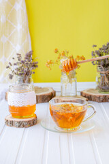 Glass cup of tea with linden in natural organic herbs and a jar of honey on a white wooden table.