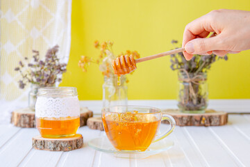 Glass cup of tea with linden in natural organic herbs and a jar of honey on a white wooden table.