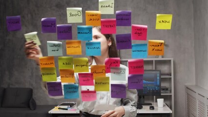 Young business woman is doing brainstorm using stickers on the glass. Office worker is thinking about strategy, business plan and goals. Startup concept.