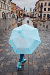 Back view of child holding big blue umbrella walking in a downtown on rainy gloomy autumn day