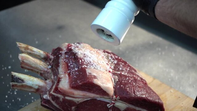  the gloved chef sprinkles peppercorns on a large piece of meat