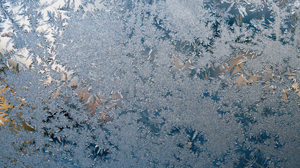 Ice and frost on the window. Blue lace winter wallpaper or background. Frozen water crystal...