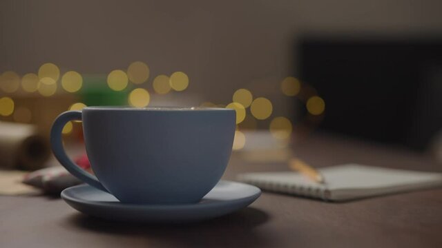 Slow motion orbit shot of man add marshmallow and straw to hot chocolate in blue cup in the evening with shopping list for holidays in notepad