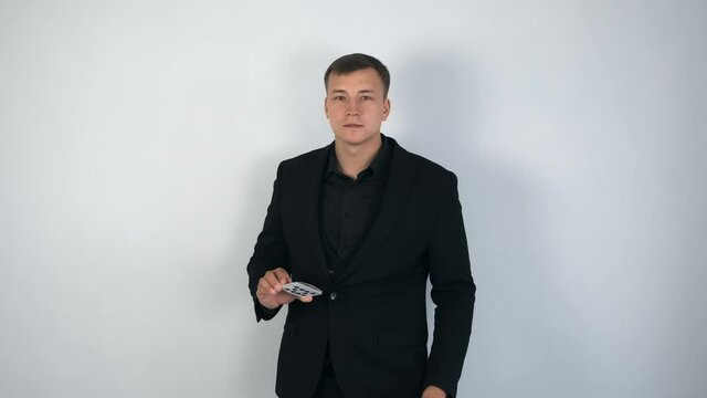 Illusionist is tryng to do trick. Magician man in black suit is making cards trick, throwing and catching cards in the air in slow motion. He is standing on grey background and looking at camera.