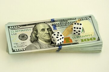 Dice on a stack of hundred-dollar bills on a white background close-up.