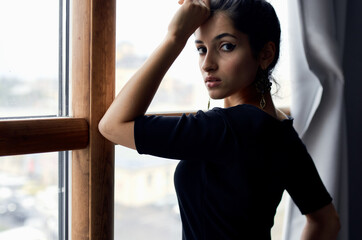 a romantic brunette in an evening dress leaned her hand on the window and gray curtains in the background