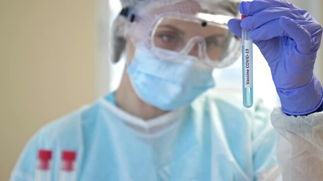 An expert works on a covid 19 coronavirus vaccine in a clean laboratory with a protective suit, gloves, goggles and a mask.