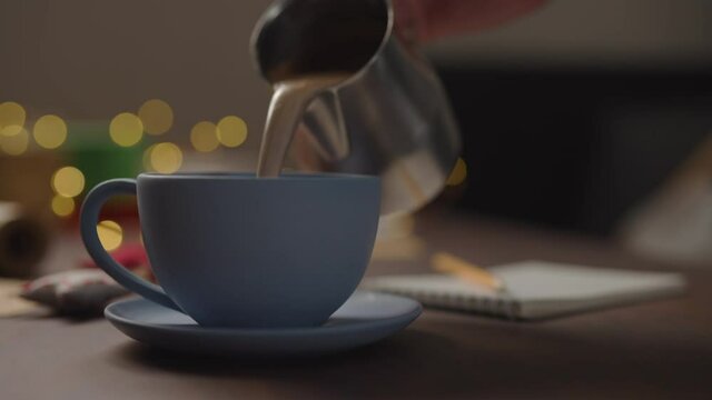 Slow motion orbit shot of man pour hot chocolate in blue cup in the evening with shopping list for holidays in notepad