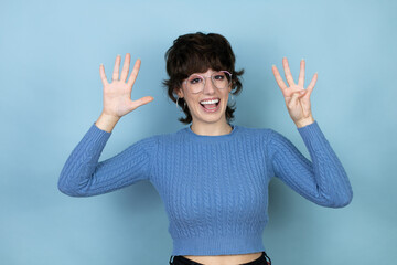 Young caucasian woman over isolated blue background showing and pointing up with fingers number...