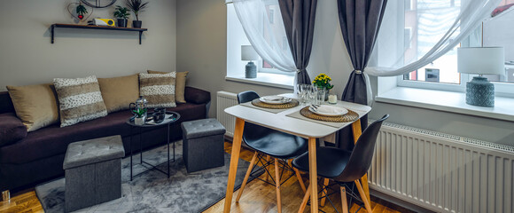 Modern interior of small studio apartment. Laid table on two persons. Cozy couch with cushions. Home decor.