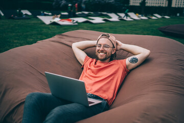 Happy carefree man using laptop while resting in park