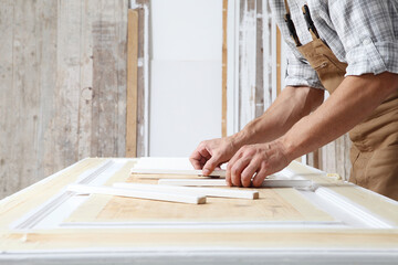 Male carpenter working the wood in carpentry workshop, putting wooden sticks on a door,  wearing...