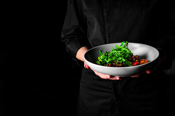 chef in a black suit holds in his hands bowl with salad on Dark grey black background