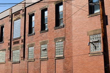 Angled view of old red brick industrial building, lower windows filled with glass block, interesting architectural details, horizontal aspect