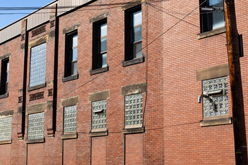 Fototapeta na wymiar Angled view of old red brick industrial building, lower windows filled with glass block, interesting architectural details, horizontal aspect