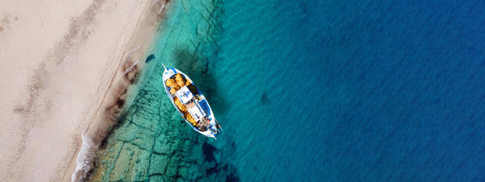 Aerial top view photo of traditional fishing boat anchored in turqoise bay and beach of Balos, Chania, Crete, Greece