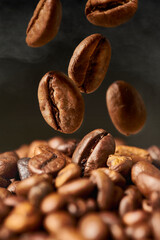 Close up of roasted coffee beans on a black smokey background. The grains fall from above in a group.