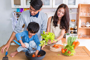 The cute boy and beautiful parents are cooking and smiling while happily cooking in the kitchen at home.