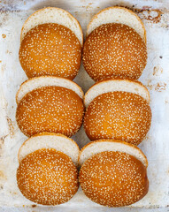 Delicious homemade fresh sesame buns cut in half for burgers close-up on an old metal baking sheet. Top view, selective focus