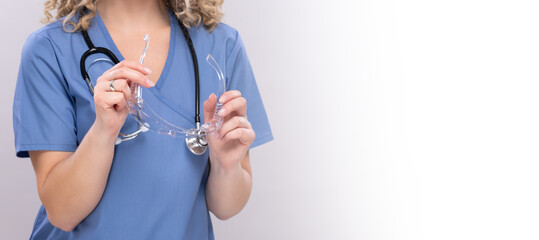 Hände einer Frau im Kittel mit Stethoskop und Schutzbrillen