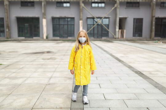 little caucasian girl 7 years old with blonde hair in yellow raincoat and face mask during Coronavirus pandemic. Colors of the year 2021 ultimate gray and illuminating