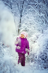 Fototapeta na wymiar A little girl looks at the fresh snow with enthusiasm. Walk in the winter forest