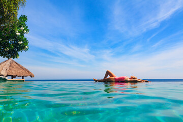 Happy girl have fun on summer beach holiday. Young woman relaxing at edge of infinity swimming pool...