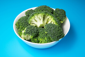 Beautiful combination of green fresh broccoli in white ceramic bowl on blue background.