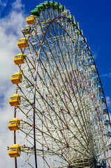 Giant Ferris wheel with views from below against blue sky white clouds