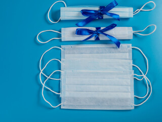 Covid-19. Medical disposable mask tied with a blue bow, on a blue background. Gift.