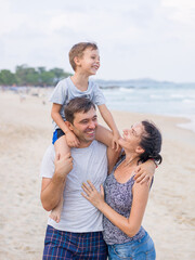 Young and beautiful mom and dad laugh and have fun with their son on the beach
