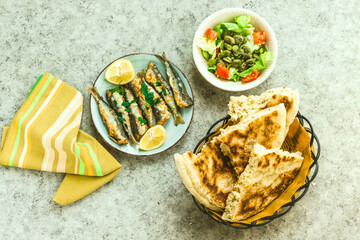 fried sardines on the plate decorated with lemon and parsley, salad bowl and Arabic bread