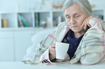 Portrait of sad old woman with headache drinking tea