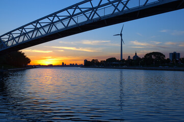 Sunset over water with wind turbine and foot bridge