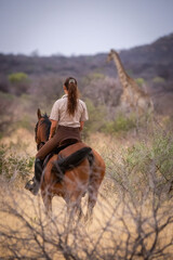 Brunette on horseback watches giraffe in bushes