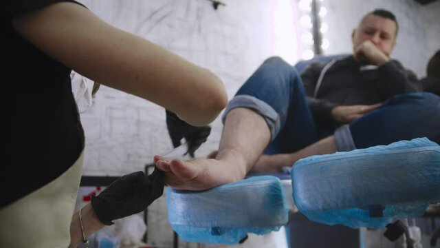 Pedicure procedure - the master in black gloves doing the toenails of her male client using a nail file