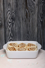 Baking cinnabons. The cinnamon dough is in the baking dish. Background from black pine boards. Close-up shot.