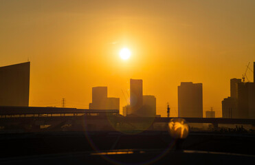 a sunset over a city skyline with tall buildings silhouetted against the bright orange sky.