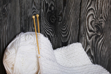 Knitting with needles. Wooden knitting needles and white threads. On black pine boards.