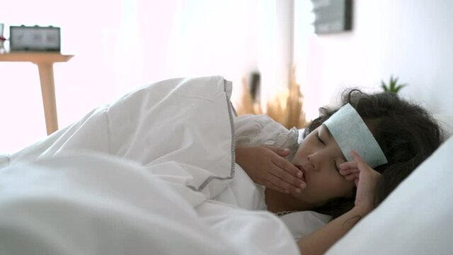 Asian young girl laying down on the bed in bedroom, a little young girl got a serious high fever from flu virus.