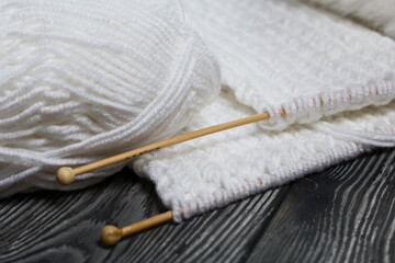 Fototapeta na wymiar Knitting with needles. Wooden knitting needles and white threads. On black pine boards.