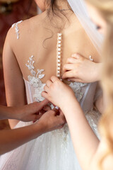 Bridesmaids preparing bride for the wedding day, helping fasten her dress